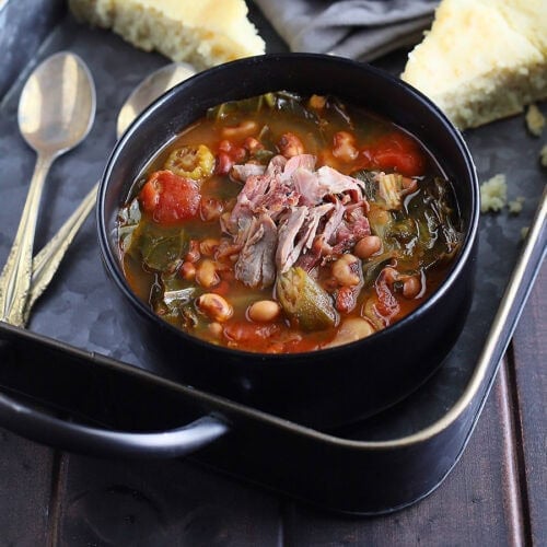 Bowl of vegetable soup with collard greens garnished with shredded ham and served with wedges of cornbread.