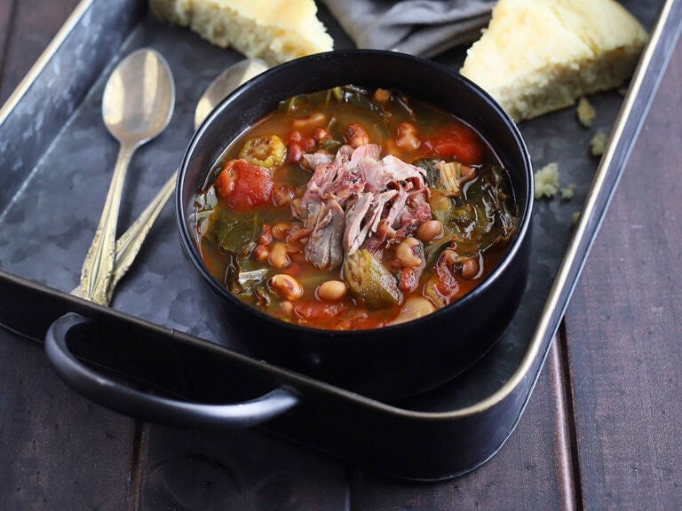 Bowl of vegetable soup with collard greens garnished with shredded ham and served with wedges of cornbread.