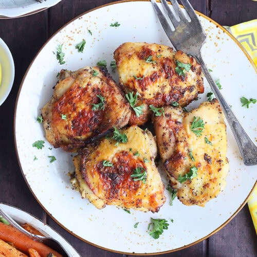 Four chicken thighs on a serving plate with a dish of collard greens and roasted carrots on the side.