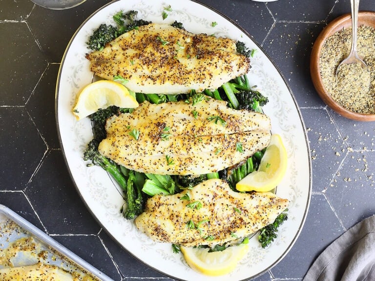 Platter of lemon pepper air fryer catfish over a bed of broccolini.