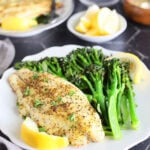 Lemon pepper air fryer catfish fillet on a plate with broccolini and lemon wedges.