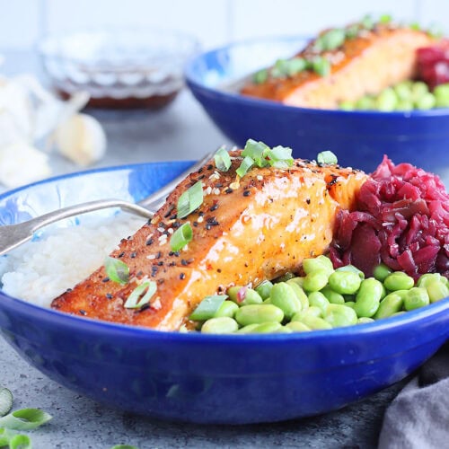 Filet of air fryer teriyaki salmon in a bowl with white rice, shelled edamame and pickled cabbage.