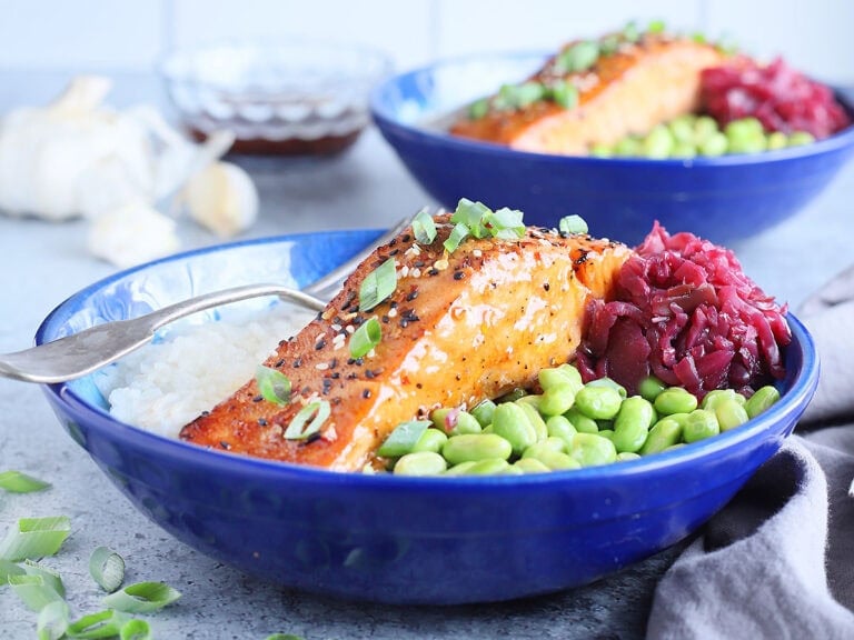 Filet of air fryer teriyaki salmon in a bowl with white rice, shelled edamame and pickled cabbage.