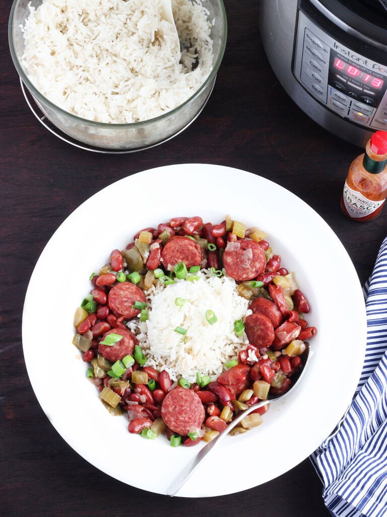 Dish of Instant Pot red beans and rice with an Instant Pot electric pressure cooker and a serving bowl of cooked rice in the background.