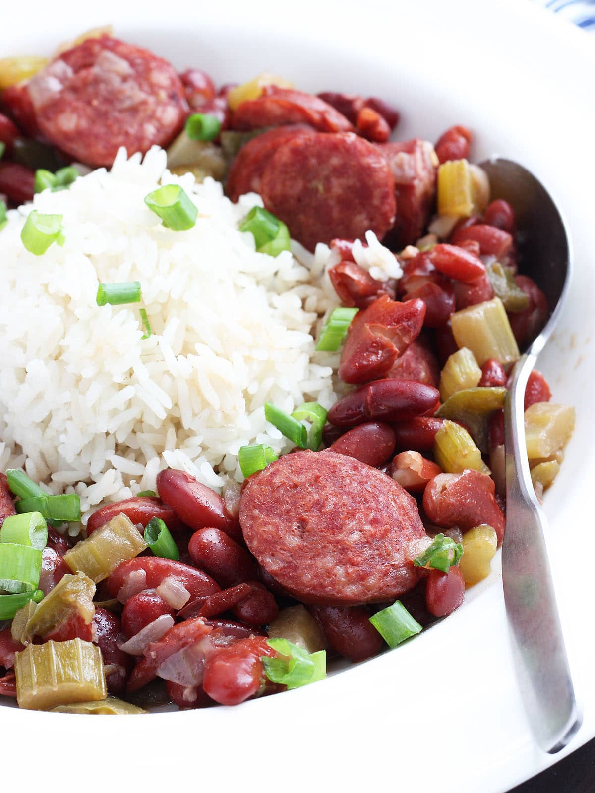 Spoon tucked into a serving of Instant Pot red beans and rice garnished with sliced green onions.