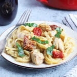 Serving of Marry Me Chicken Pasta with a glass of red wine and a serving bowl of pasta in the background.
