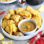 Platter of catfish nuggets with champagne dipping sauce on the side served with French fries and cole slaw.
