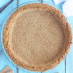 Baked graham cracker pie crust with a pie server, napkins and broken graham crackers to the side.