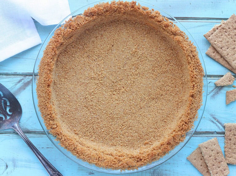 Baked graham cracker pie crust with a pie server, napkins and broken graham crackers to the side.