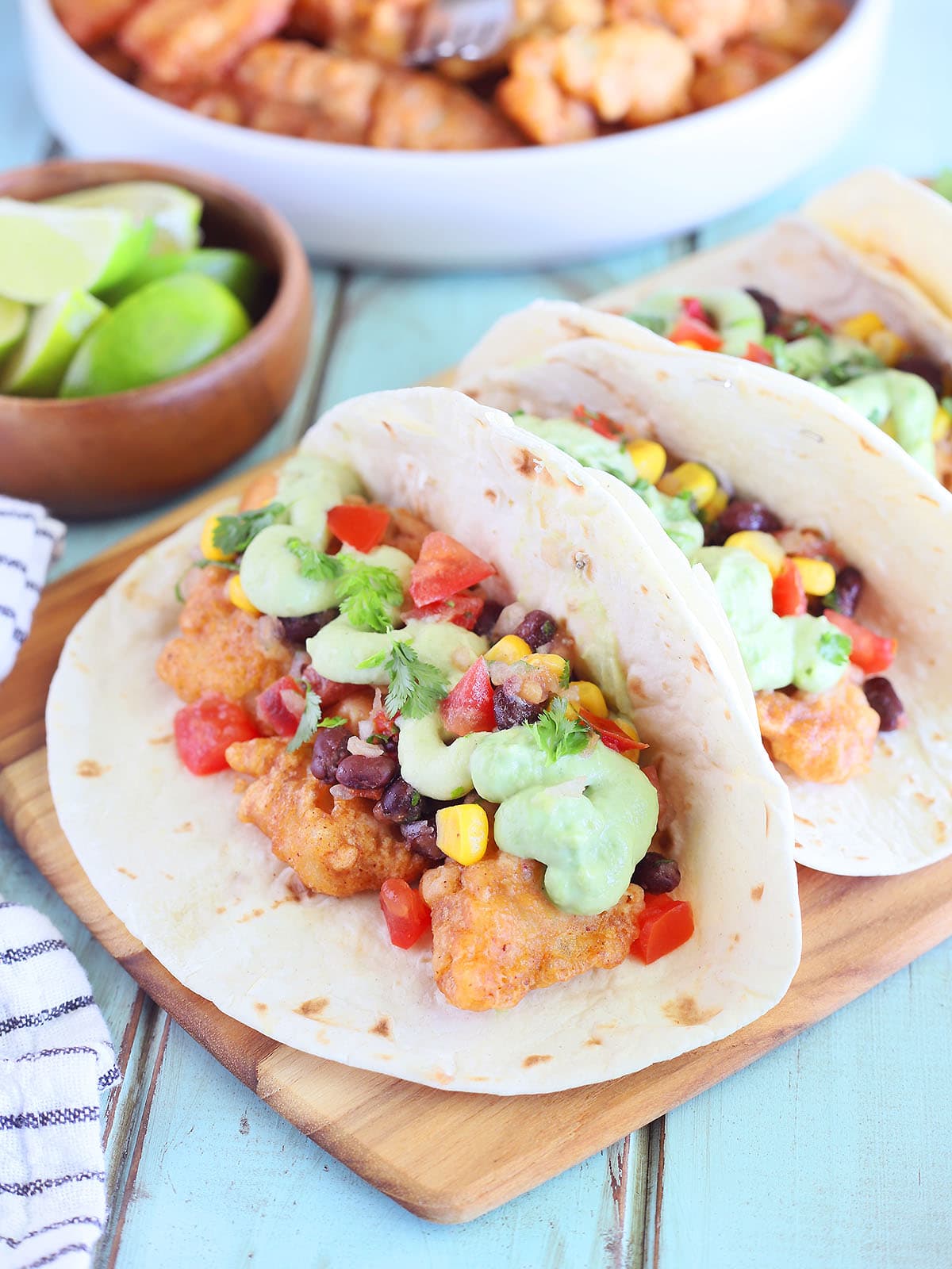 One catfish taco garnished with avocado cream sauce and salsa on a wooden cutting board.