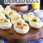 Crab deviled eggs garnished with crab meat, paprika and fresh chives on a wooden cutting board.