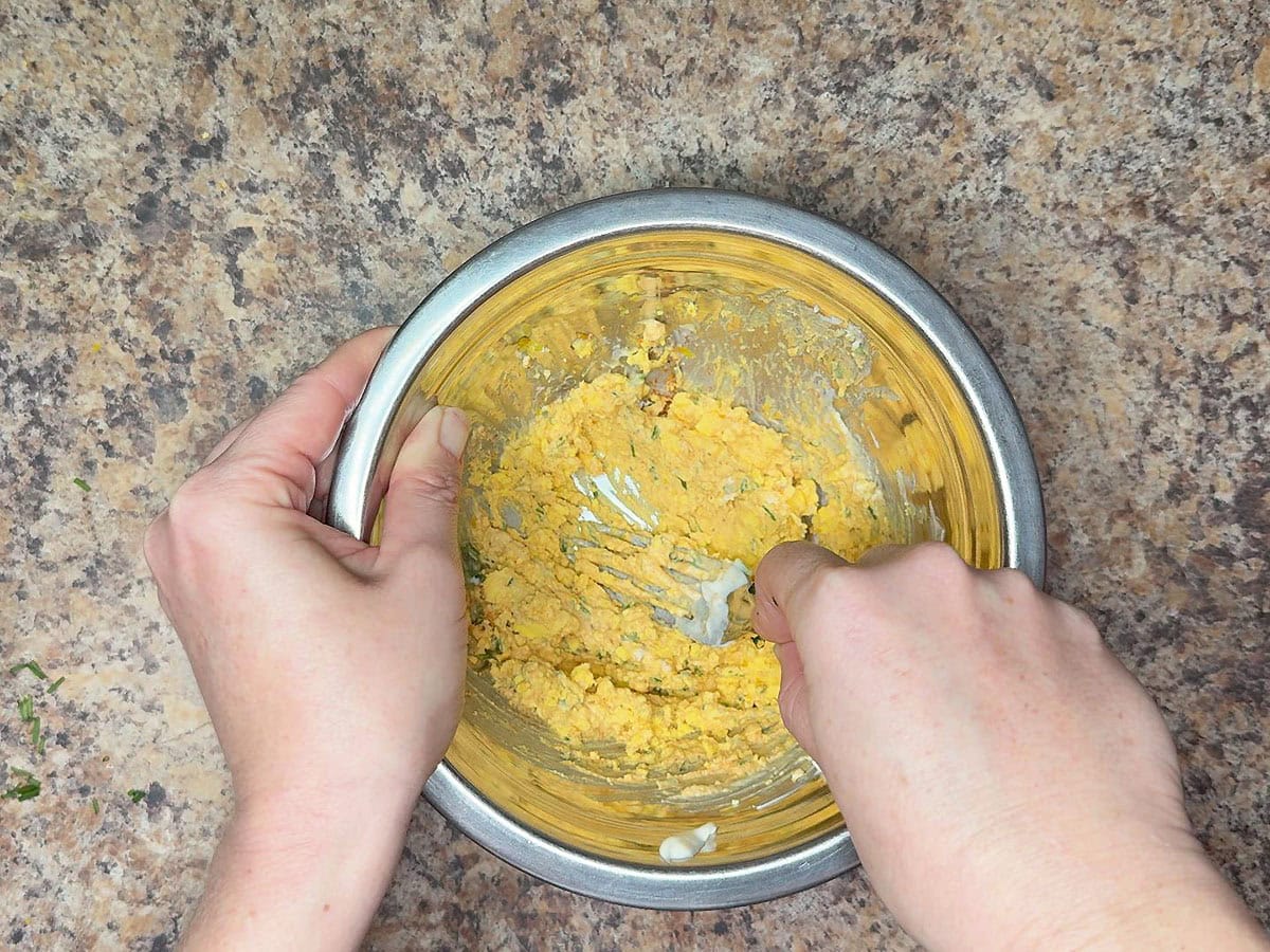 Mashing the egg yolks with the mayonnaise, Dijon mustard, Old Bay seasoning, lemon zest, hot sauce, and chopped fresh chives.