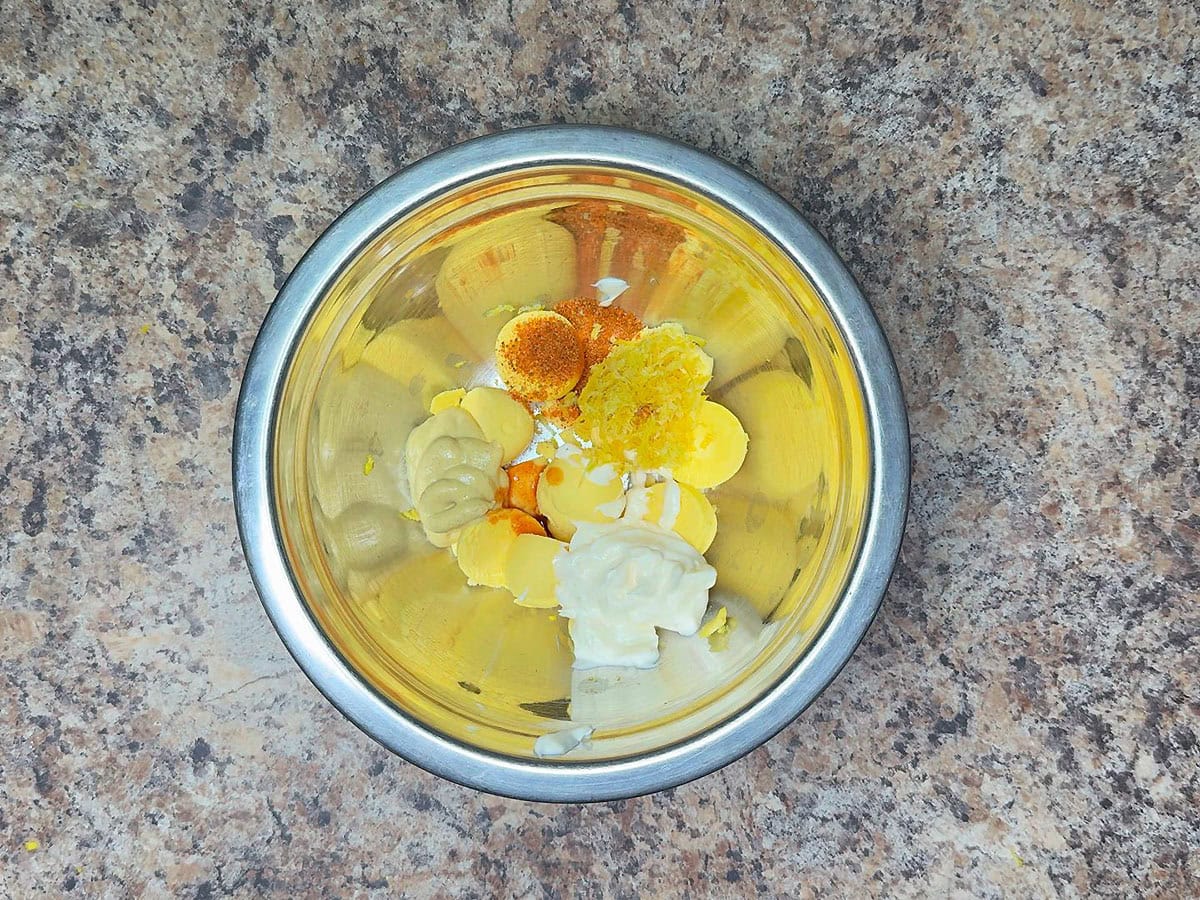 Egg yolks, mayonnaise, Dijon mustard, Old Bay seasoning, lemon zest, and hot sauce in a medium mixing bowl.
