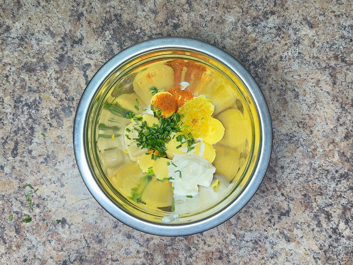 Egg yolks, mayonnaise, Dijon mustard, Old Bay seasoning, lemon zest, hot sauce, and chopped fresh chives in a medium mixing bowl.