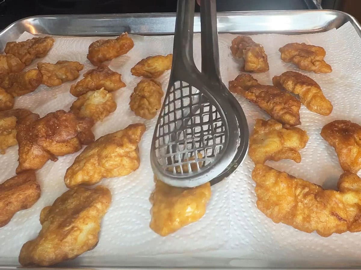 Tongs removing a piece of fish from the hot oil and placing it on a paper towel.