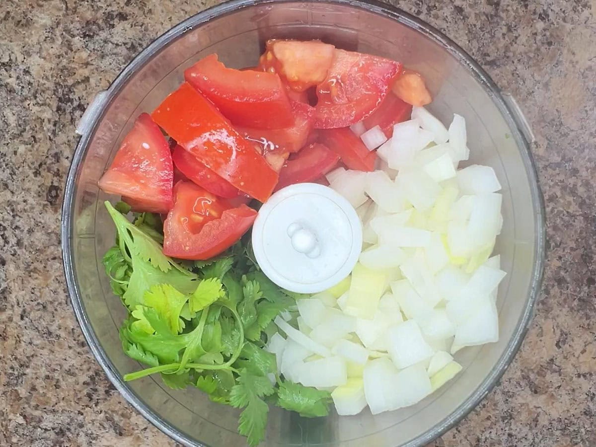 Large pieces of tomato, cilantro and onion in a food processor before it has been chopped.