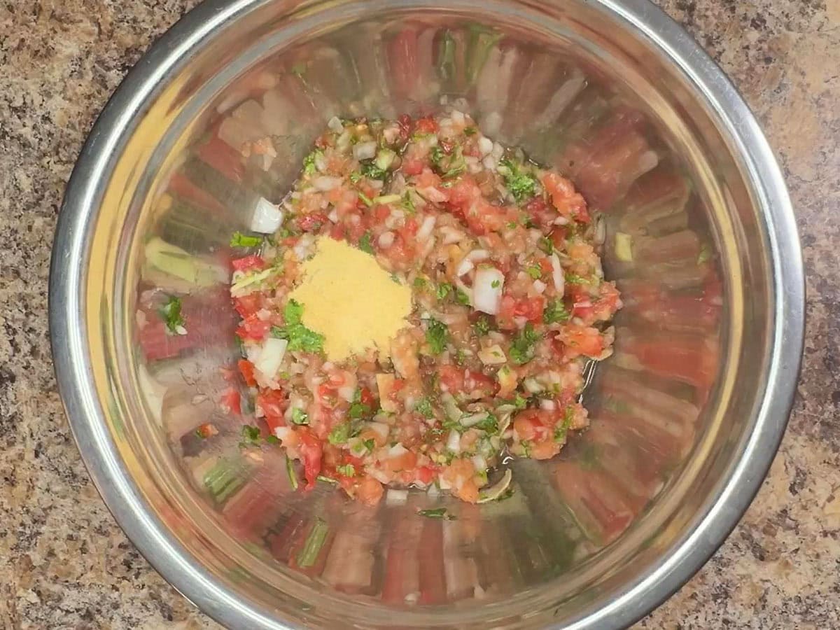 Garlic powder added to the salsa ingredients in a mixing bowl.