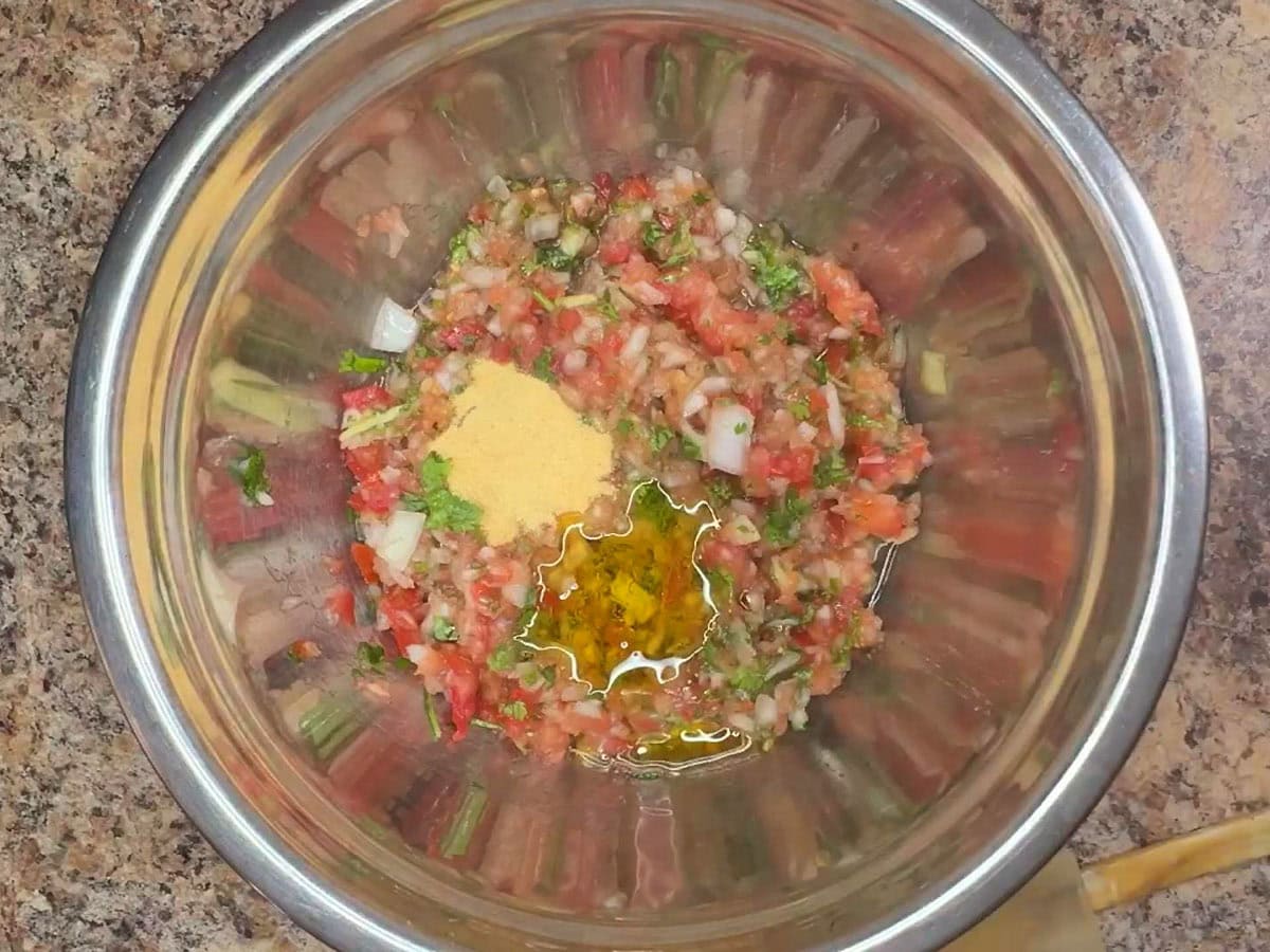 Olive oil added to the salsa ingredients in a mixing bowl.