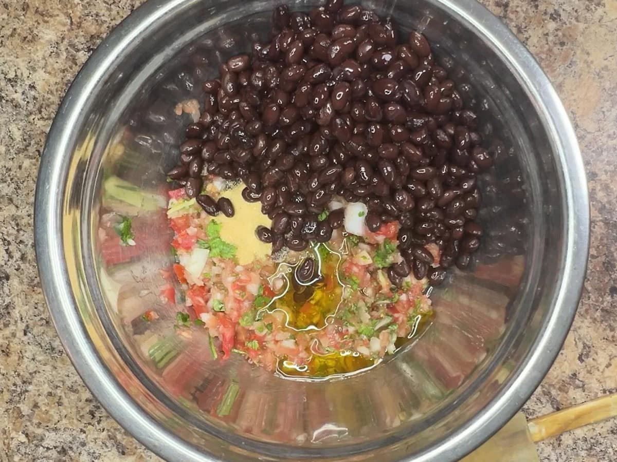 Black beans added to the black bean salsa ingredients in a mixing bowl.