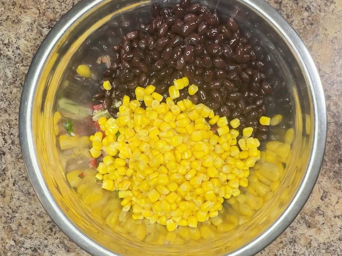 Corn added to the black bean salsa ingredients in a mixing bowl.