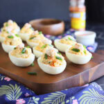 Crab deviled eggs garnished with crab meat, paprika and fresh chives on a wooden cutting board.