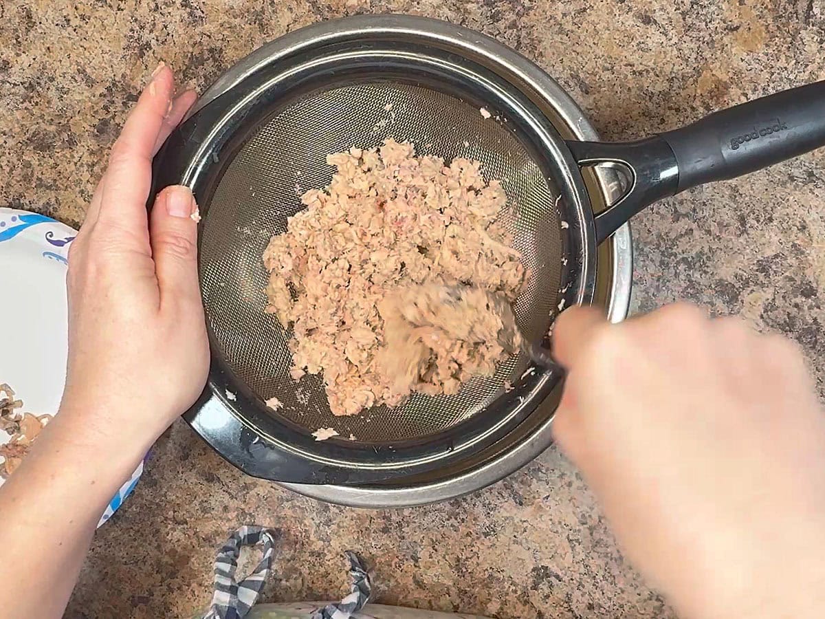 Hands picking through the canned salmon in a strainer to remove any large pieces of skin and bone.