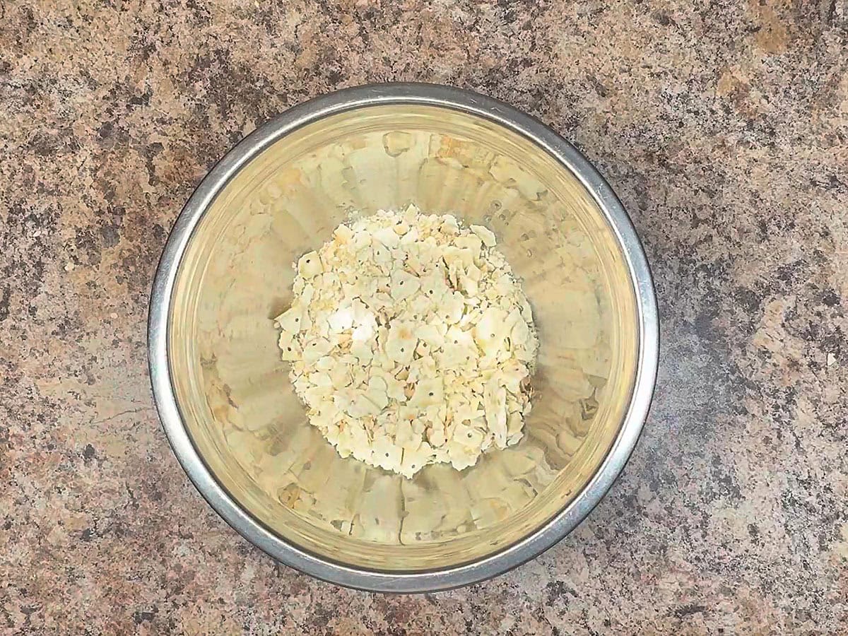 Crushed saltine crackers in a large mixing bowl with the juice from the can of salmon.