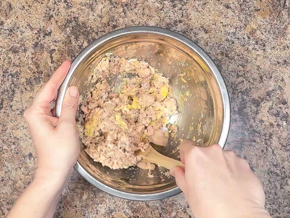 Hands using a wooden spoon to mix the salmon croquette mixture together.