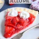 Slice of strawberry pie with jello topped with whipped cream on a plate with a fork on the side.
