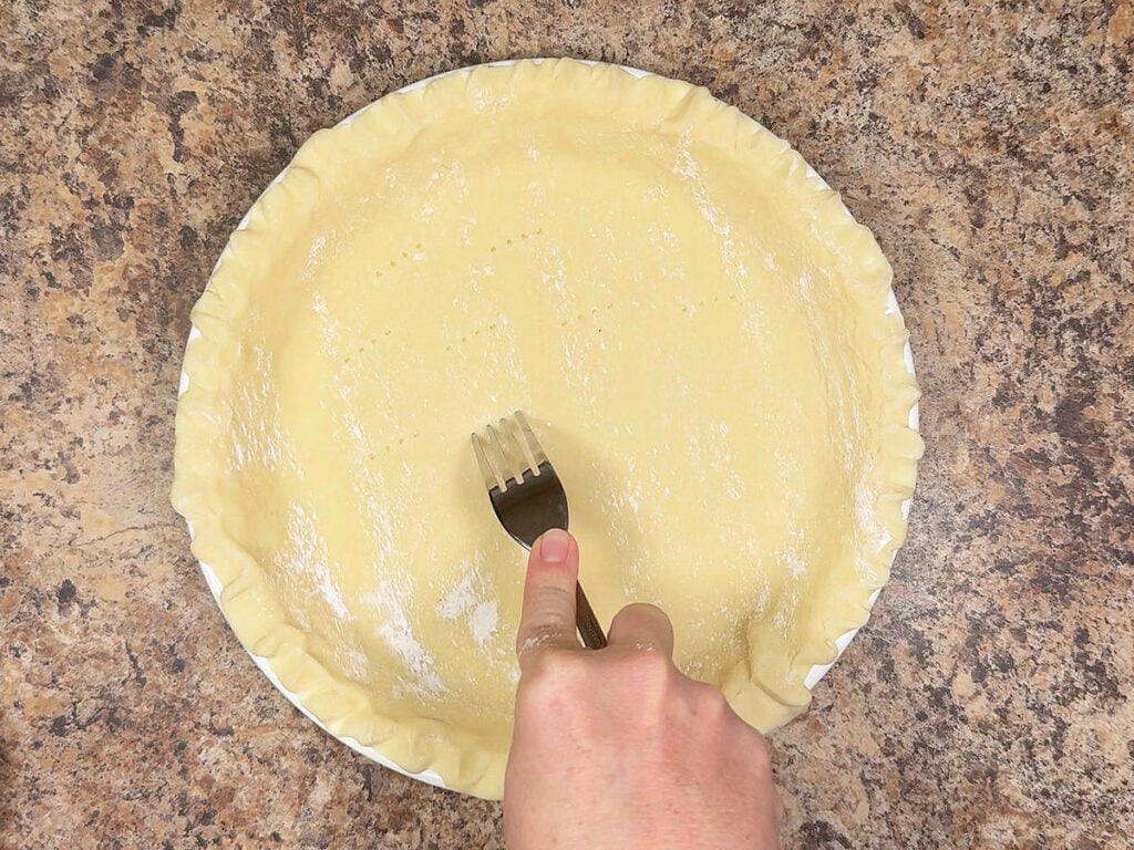 Docking an unbaked pie crust with a fork before baking.
