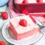 Single slice of strawberry sheet cake garnished with a fresh strawberry slice on a plate with a fork to the side.