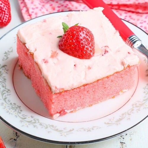 Single slice of strawberry sheet cake garnished with a fresh strawberry slice on a plate with a fork to the side.