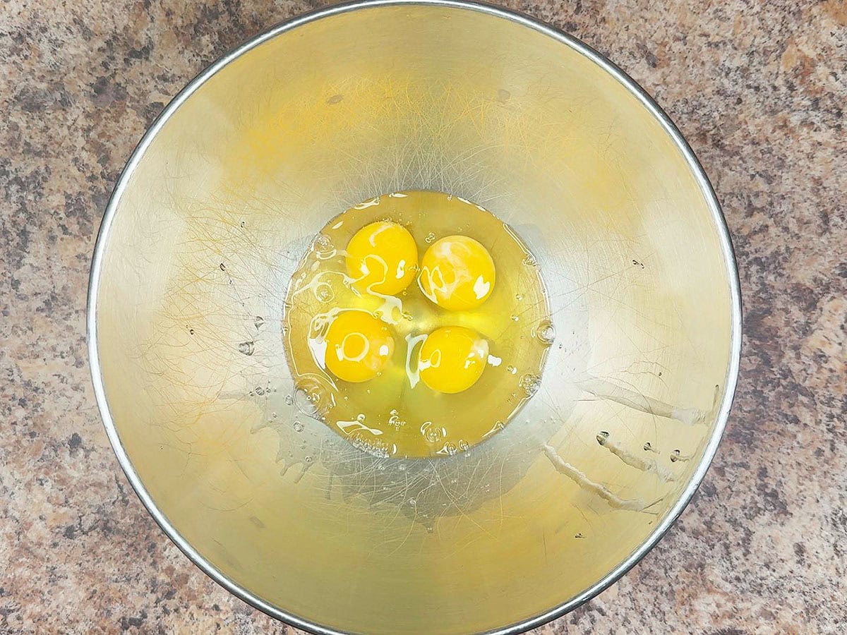 Four eggs in a large mixing bowl.