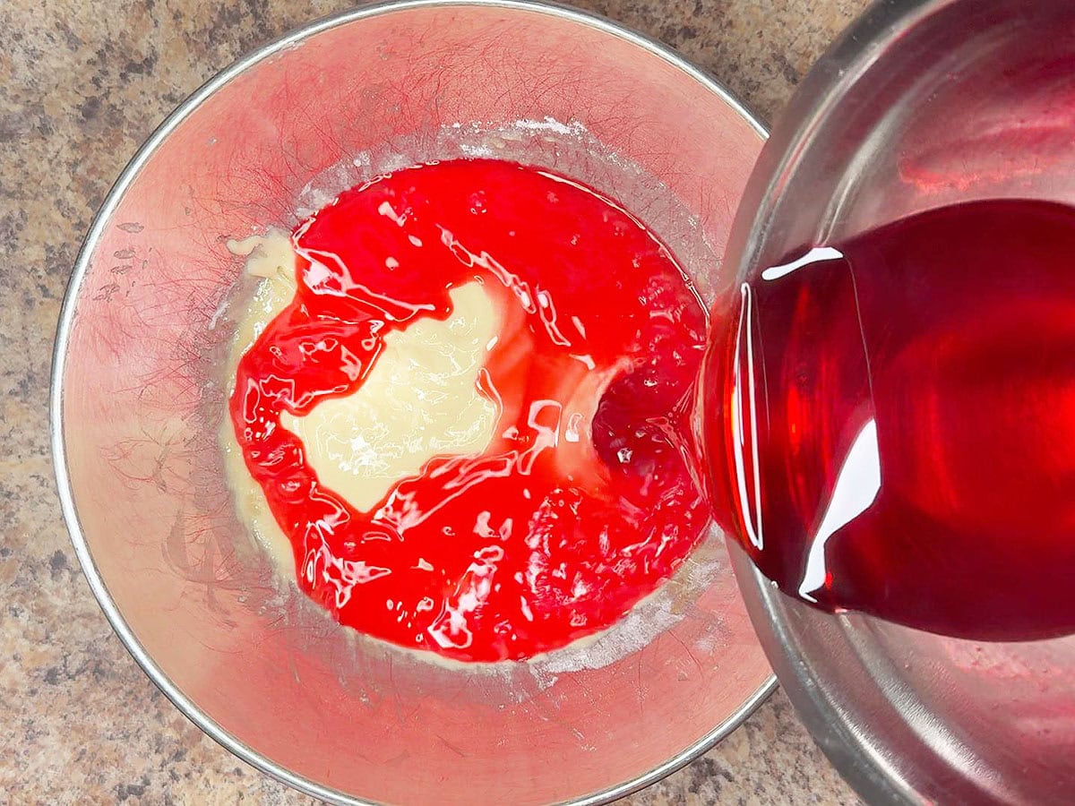 Pouring strawberry gelatin into the cake batter.