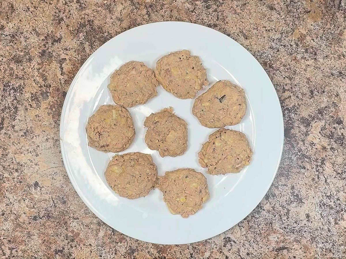 Eight uncooked salmon patties on a large plate.
