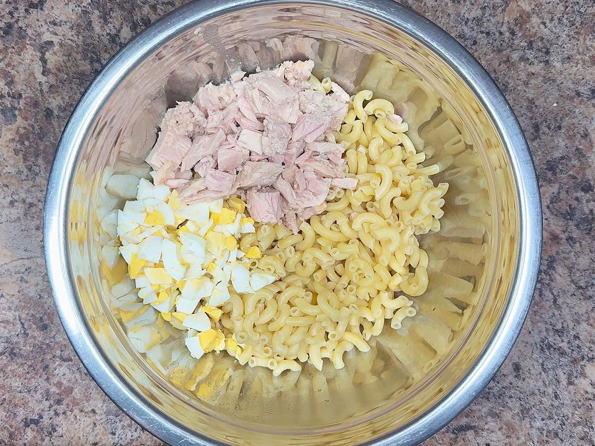 Cooked macaroni noodles, chopped hard boiled eggs, and chunks of tuna in a large mixing bowl.