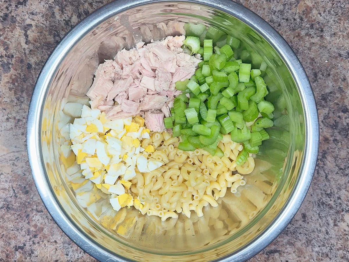 Cooked macaroni noodles, chopped hard boiled eggs, chunks of tuna, and diced celery in a large mixing bowl.