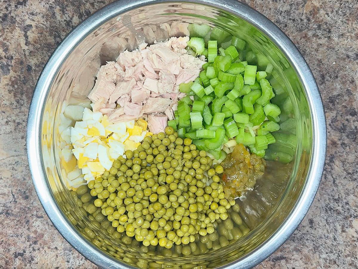 Cooked macaroni noodles, chopped hard boiled eggs, chunks of tuna, diced celery, sweet peas, and pickle relish in a large mixing bowl.