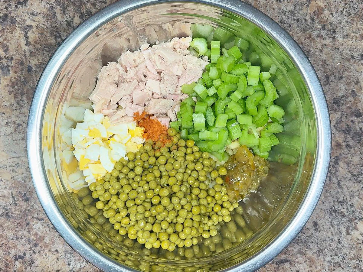 Cooked macaroni noodles, chopped hard boiled eggs, chunks of tuna, diced celery, sweet peas, pickle relish, and cayenne pepper in a large mixing bowl.