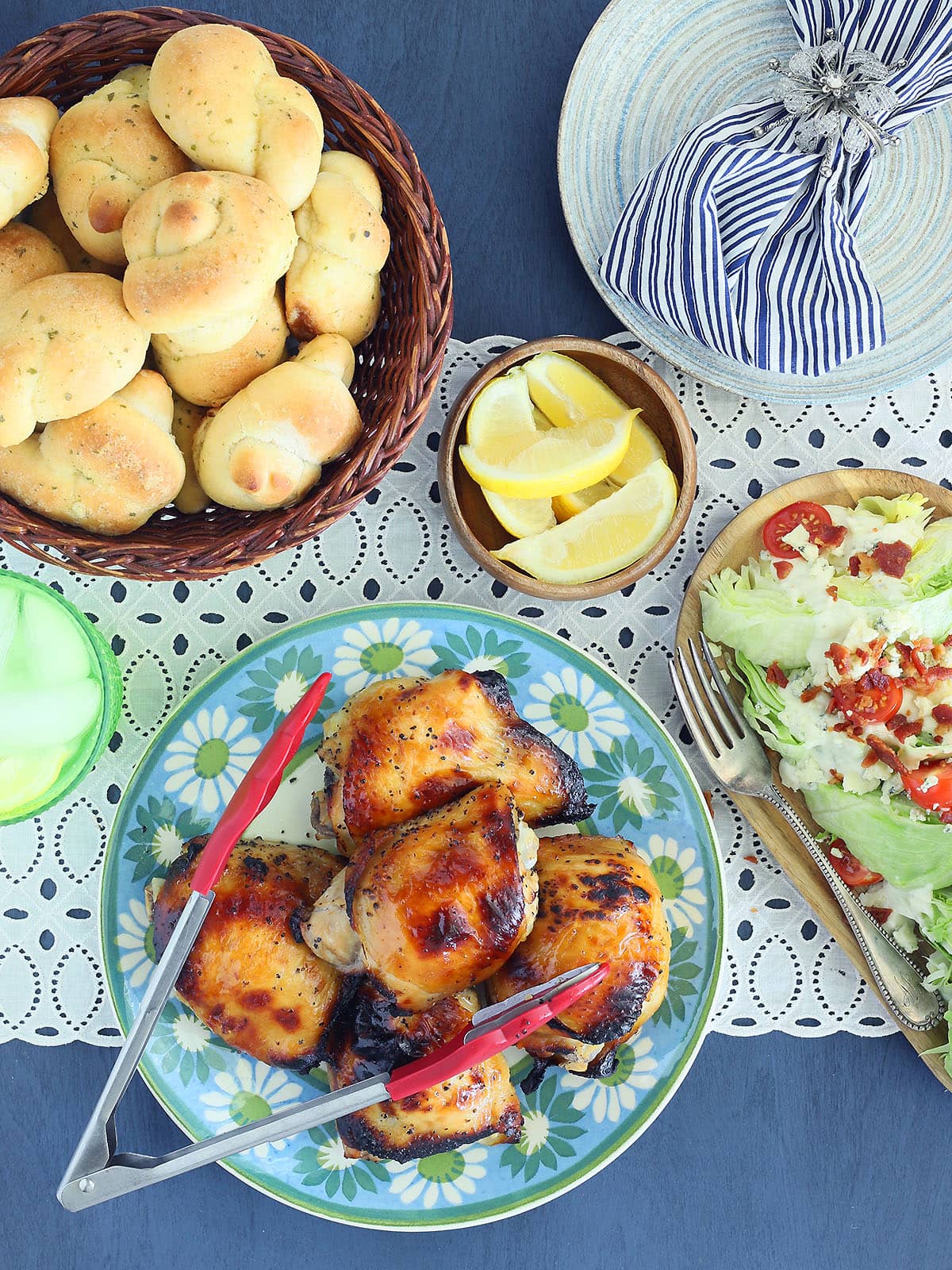 Platter of apple cider vinegar chicken with a basket of garlic knots and a platter of wedge salads on the side.
