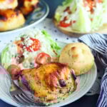 Apple cider vinegar chicken thigh on a plate with a wedge salad and garlic knot.