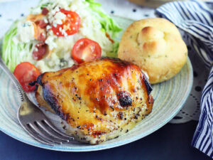 Apple cider vinegar chicken thigh on a plate with a wedge salad and garlic knot.