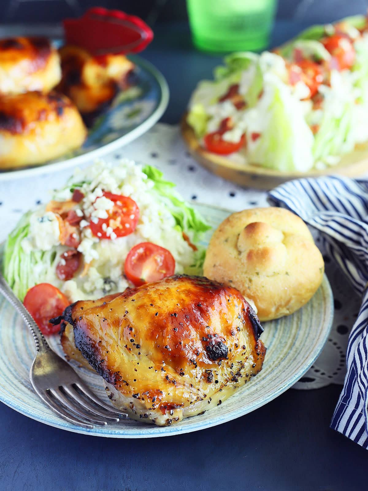Apple cider vinegar chicken thigh on a plate with a wedge salad and garlic knot.