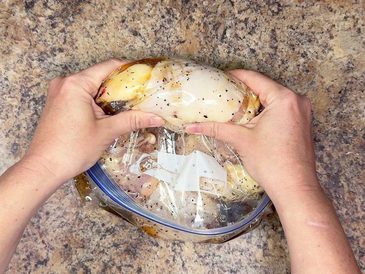 Gently shaking the bag of marinating chicken thighs to coat the meat with the marinade.