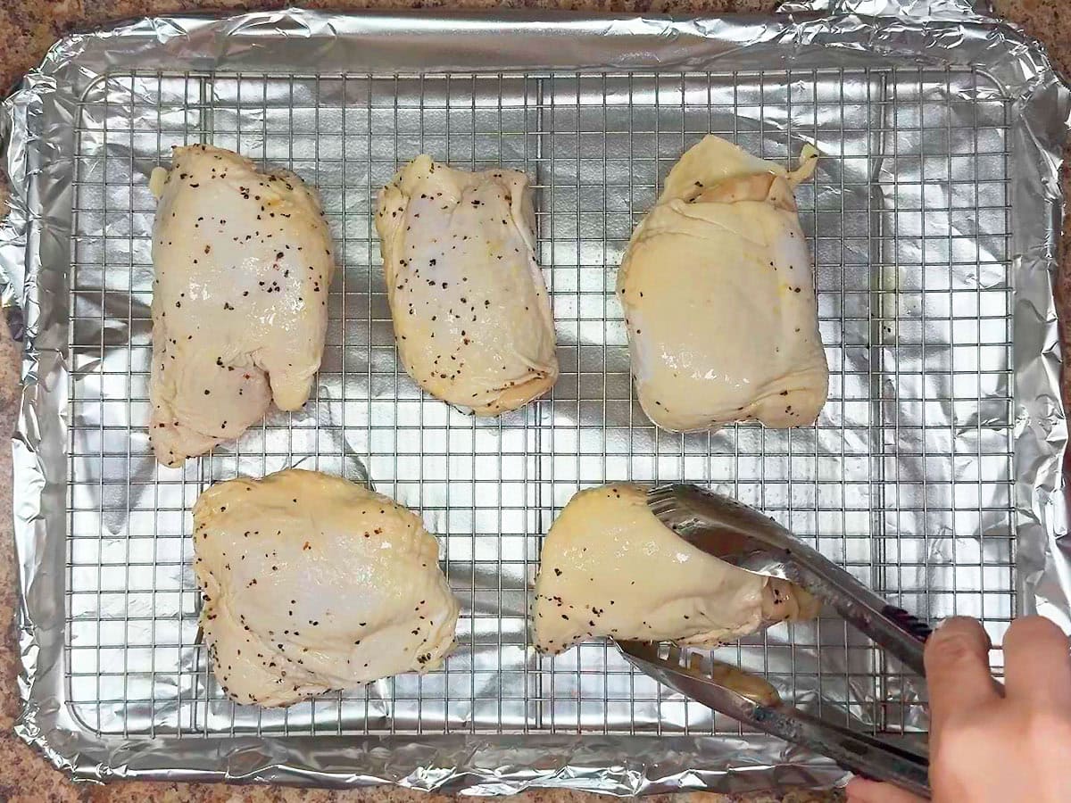 Arranging the chicken thighs on a foil lined baking sheet fitted with a greased baking rack.