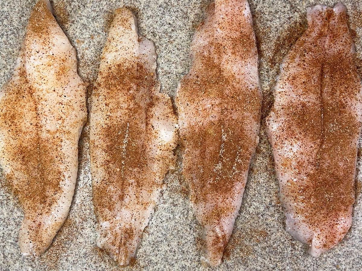 Uncooked seasoned catfish fillets on a cutting board.