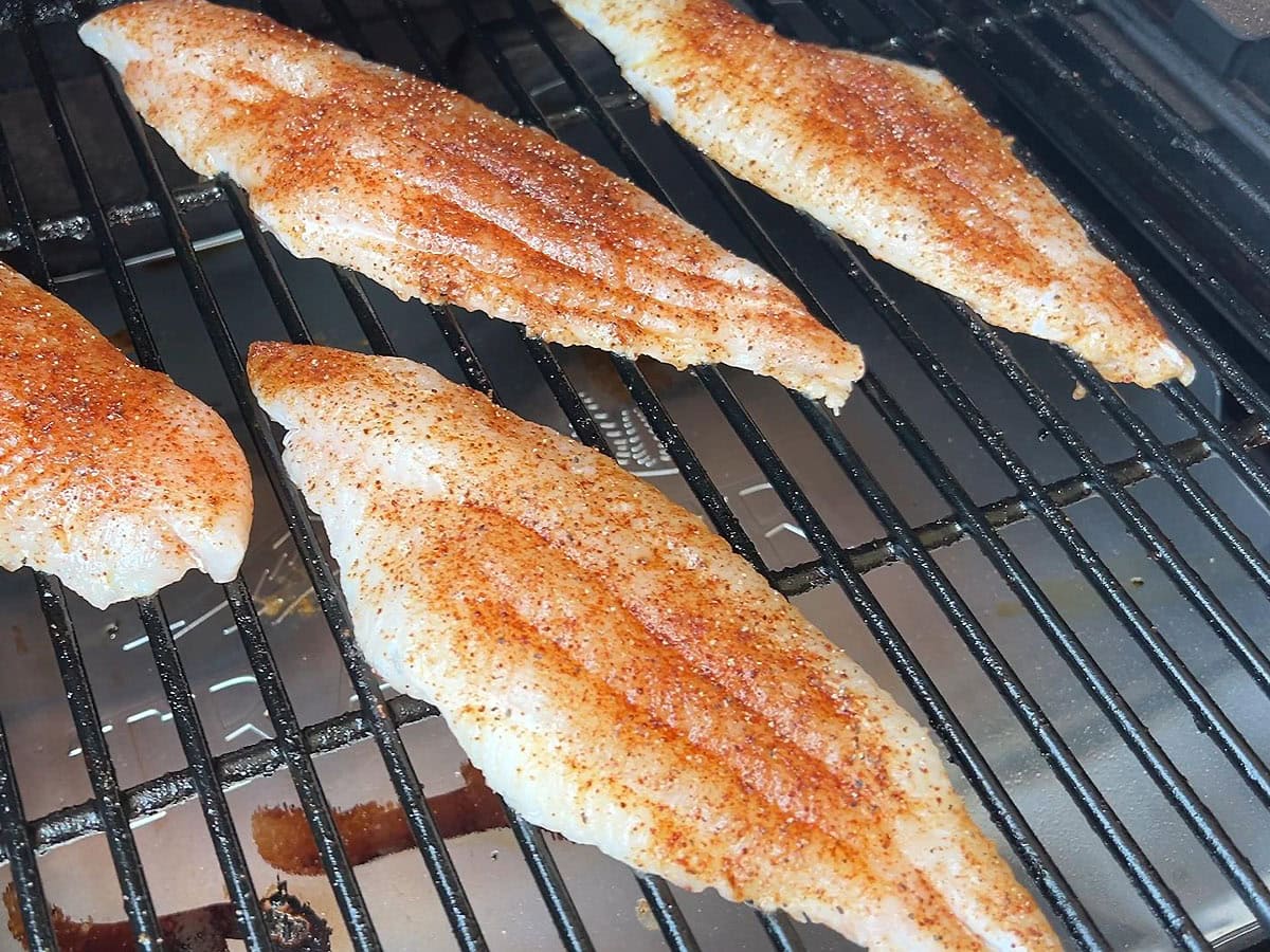 Seasoned catfish fillets cooking on a grill grate.
