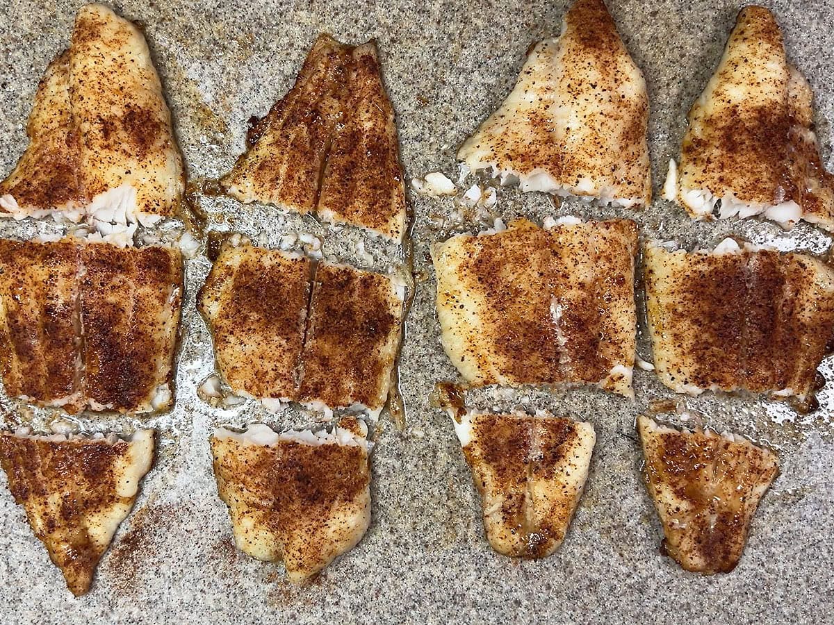 Seasoned and grilled catfish fillets each cut into three pieces on a cutting board.