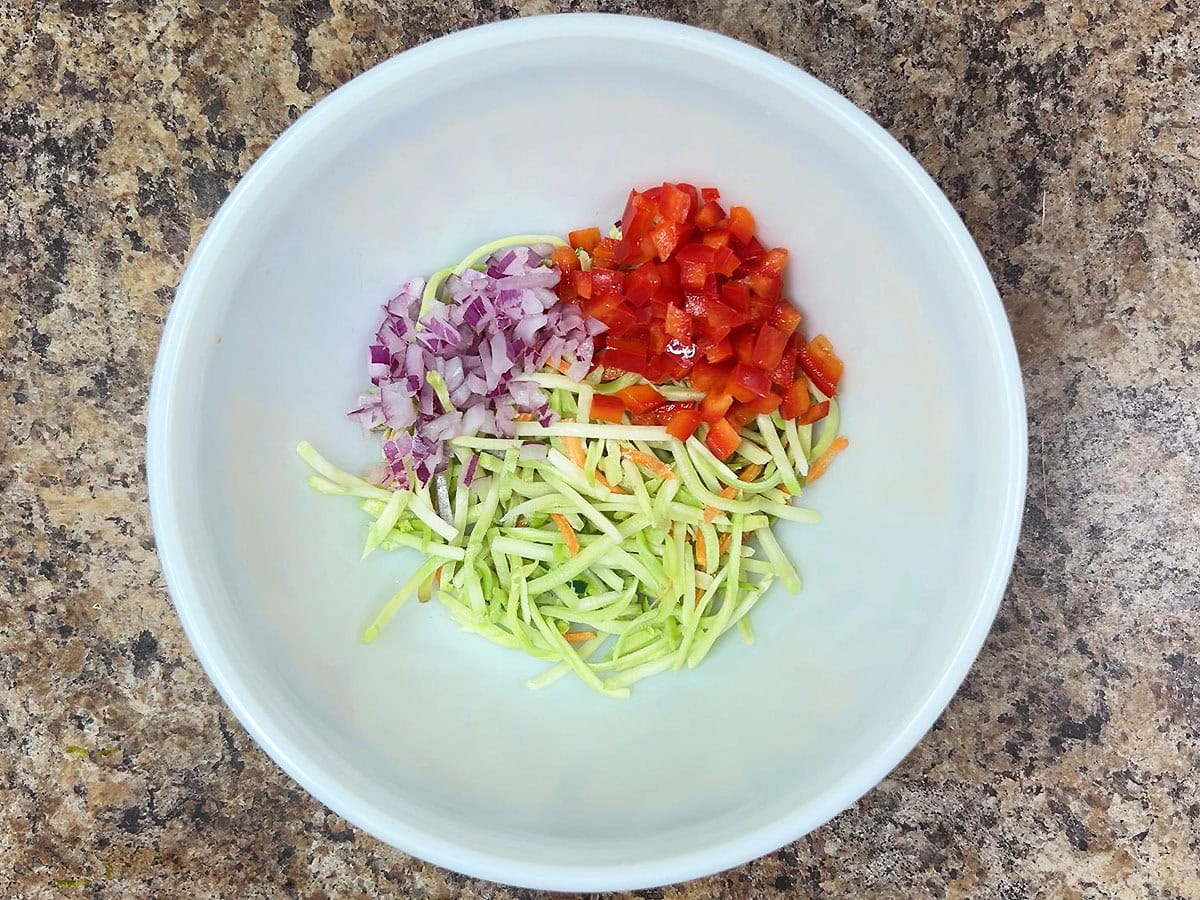 Coleslaw mix, diced red bell pepper, and diced red onion in a mixing bowl.