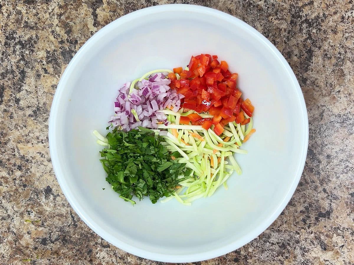 Coleslaw mix, diced red bell pepper, diced red onion, and chopped cilantro in a mixing bowl.